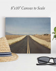 The Offley Green 8x10 Rustic Canvas Print features a straight road in a rural landscape. Nearby, charm is added with a straw hat, black sunglasses, and potted plant. Text above states "8x10 Canvas to Scale." Choose from 10+ designs.