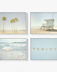 The Offley Green Set of 4 Framed Canvas 24x30 showcases palm trees on sand, a beach lifeguard tower, ocean waves, and lights spelling "VENICE," all in a soft botanical style and muted palette.