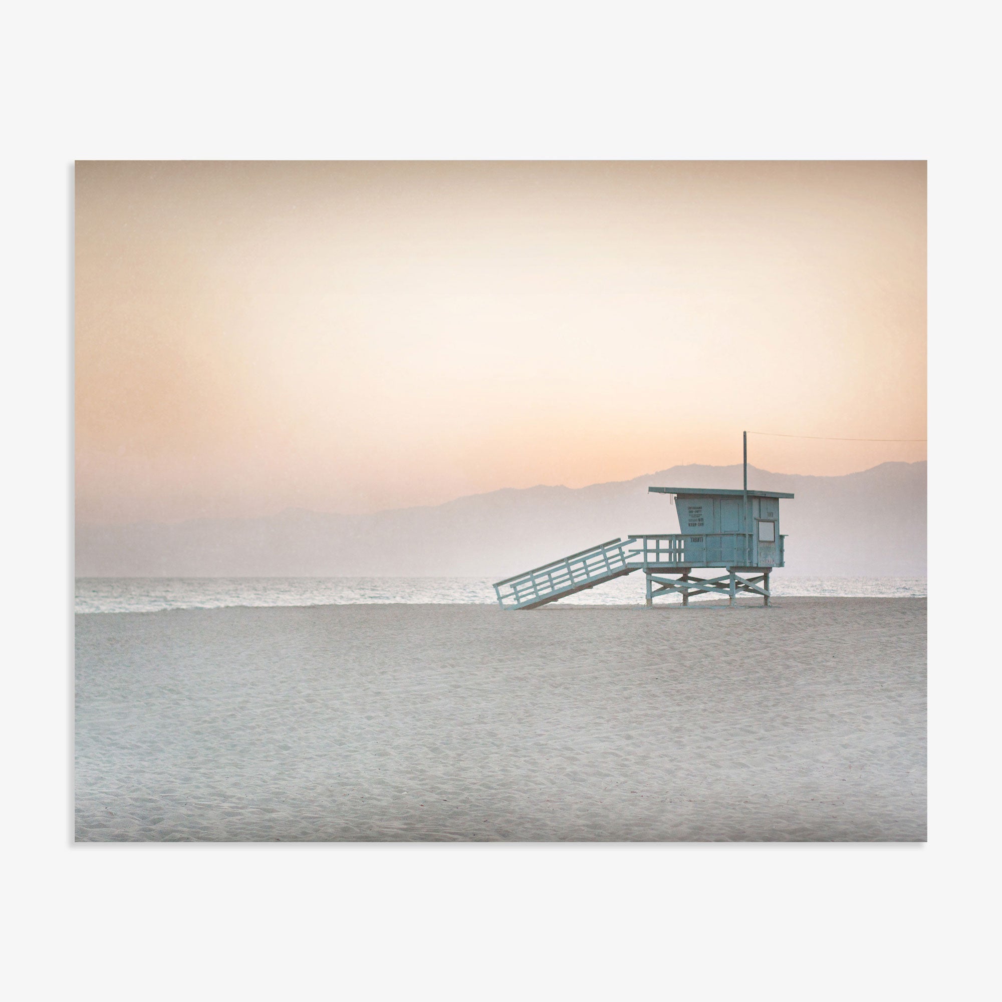 A Pink Coastal Print, 'Lifeguard Tower' by Offley Green stands isolated on a sandy beach in Venice with a calm sea in the background under a soft gradient sky of pastel colors at dawn or dusk.