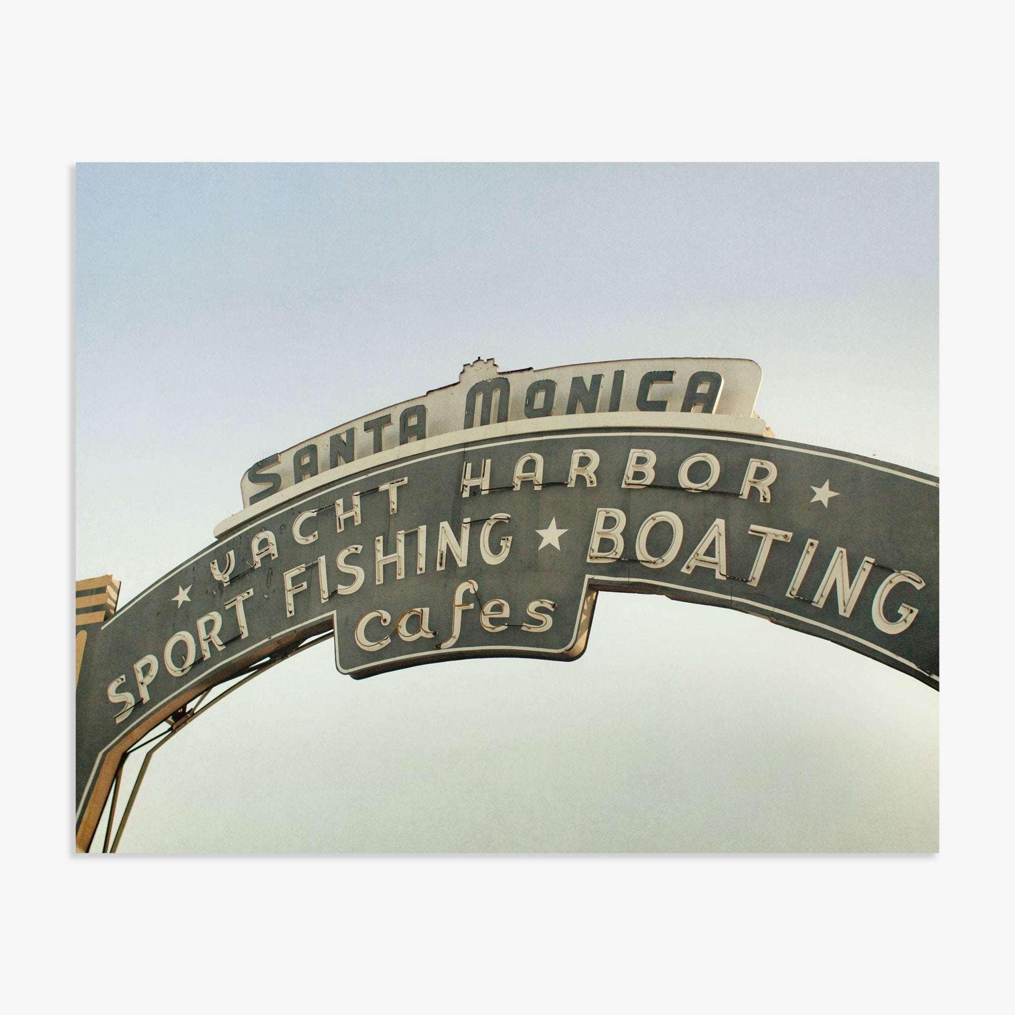 The image shows the iconic Santa Monica Pier arch sign with the text "yacht harbor, sport fishing, boating, cafes" against a clear sky on the Los Angeles California Print, 'Santa Monica Pier Blues' by Offley Green.