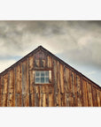 Offley Green's Farmhouse Rustic Print, 'Old Barn at Bodie', with weathered planks and a single window under a cloudy sky. The building's peak features intricate detailing against the backdrop of the Sierra Nevada mountains.