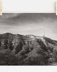 Black and white film noir photograph of the Offley Green Hollywood Sign Black and White Vintage Print, 'Old Hollywood' pinned up, set against a backdrop of a leafy hill with broadcasting antennas. The image has a rustic and vintage feel.