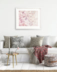 A cozy living room corner with a white sofa adorned with patterned cushions, a pink and gray throw blanket, a small round glass table, a decorative birdcage, and the Offley Green Pink Floral Print, 'Dreamy Blossom.'