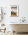 A bathroom exudes rustic charm with a vintage-style clawfoot bathtub and faucet, a wooden stool with towels and soap, a towel on a hook, and Offley Green's Rustic Farmhouse Wall Art, 'Old Wagon', adorning the wall.