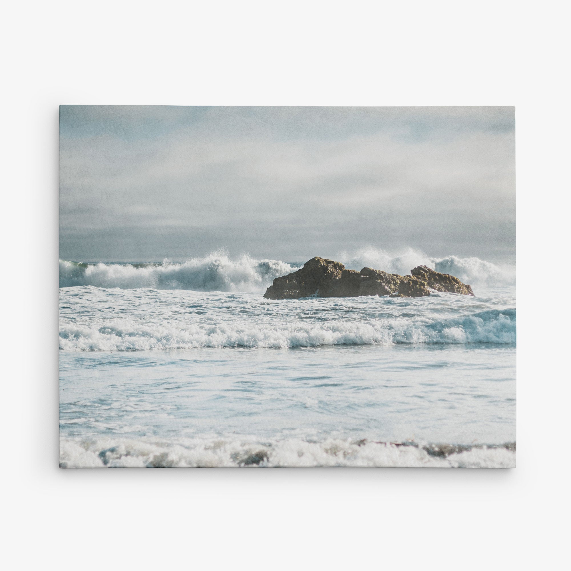A serene view of a rocky outcrop in the ocean, surrounded by foamy waves. The sky above is overcast with a layer of mist, creating a peaceful and slightly moody atmosphere. Ideal for Offley Green's 30x40 Coastal Canvas Print (Choose from 10+ Designs), the distant horizon blends softly into the sky, perfect for coastal prints or a canvas gallery wrap.