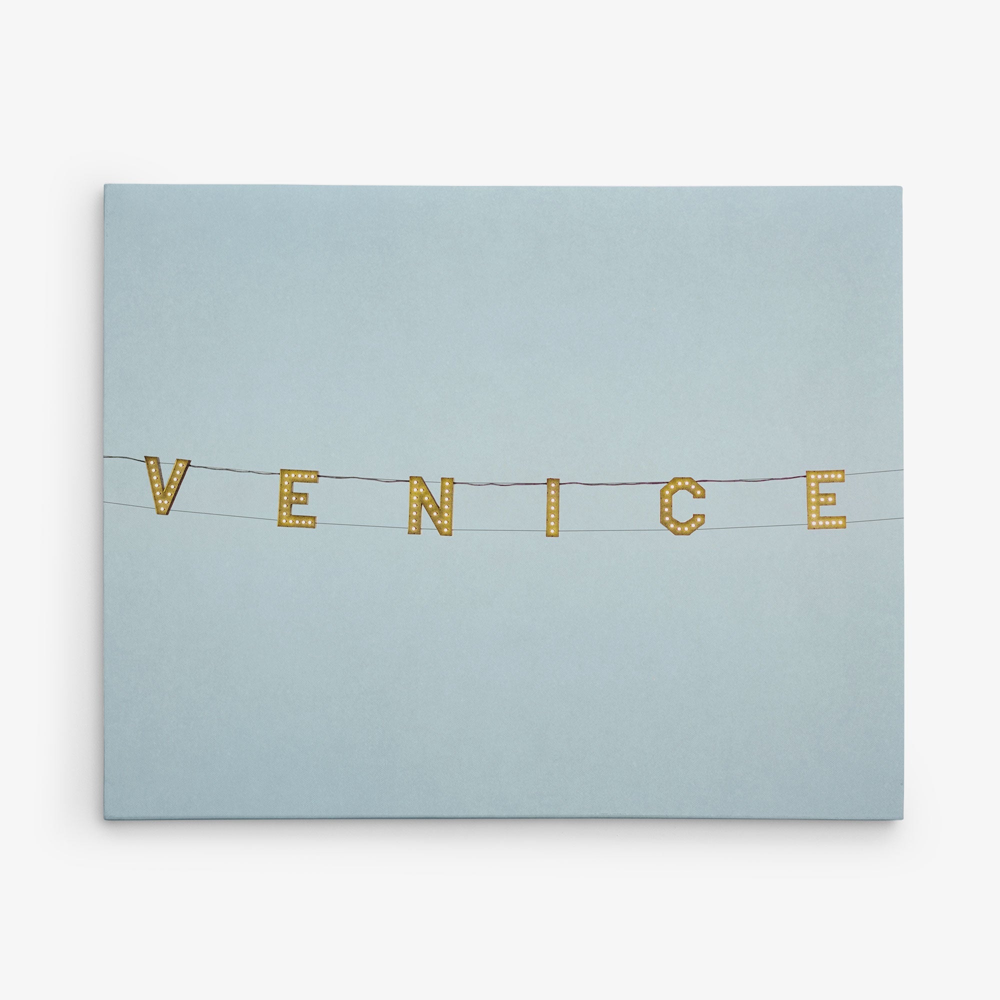 A light blue sky serves as the backdrop to the word "VENICE," spelled out in large, yellow marquee lights hanging from black wires, creating captivating wall art that embodies the vibrant spirit of Offley Green's 16x20 California Canvas Print (Choose from 10+ Designs).