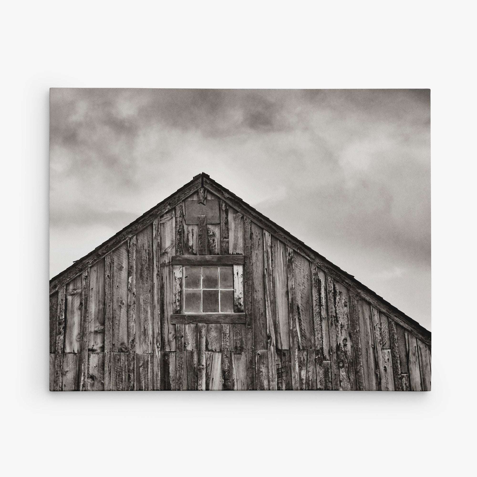 The 8x10 Rustic Canvas Print by Offley Green features a monochrome image of a rustic wooden barn with a multi-pane window and dramatic cloudy skies, perfect for creating evocative rustic prints. Choose from 10+ designs.