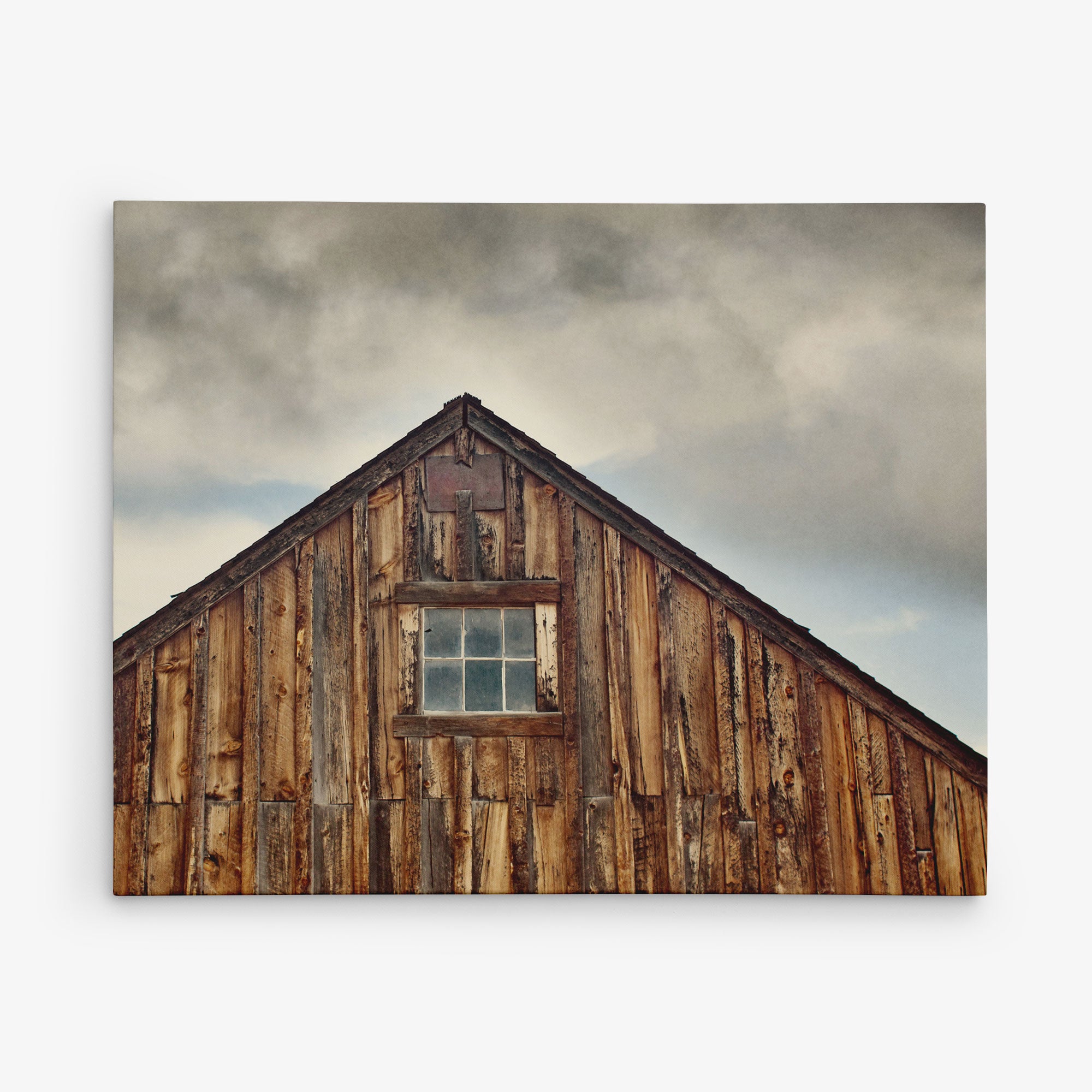 The image shows the weathered wooden roof of a rustic barn against a cloudy sky. The peak of the roof features a small, rectangular window with divided panes, highlighting the texture and aged appearance of the barn's wood—perfect for creating stunning Offley Green 11x14 Rustic Canvas Print (Choose from 10+ Designs).