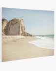 A serene beach scene with waves gently lapping at the shore and a large rocky cliff in the background under a clear blue sky, beautifully capturing Point Dume. This California Malibu Canvas Wall Art, 'Point Dume' by Offley Green is perfect as a canvas gallery wrap to bring tranquility into any room.