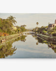 Title: A Channel of Tranquility
Description:
A serene canal with calm water beautifully reflects houses, trees, and a white arched bridge under a clear sky. Two small boats are moored along the canal's edge, while lush greenery lines both sides of the waterway—ideal for your living space. Capture this tranquil scene with the 8x10 California Canvas Print from Offley Green. Choose from 10+ designs to complement your decor perfectly as canvas gallery wrap wall art.