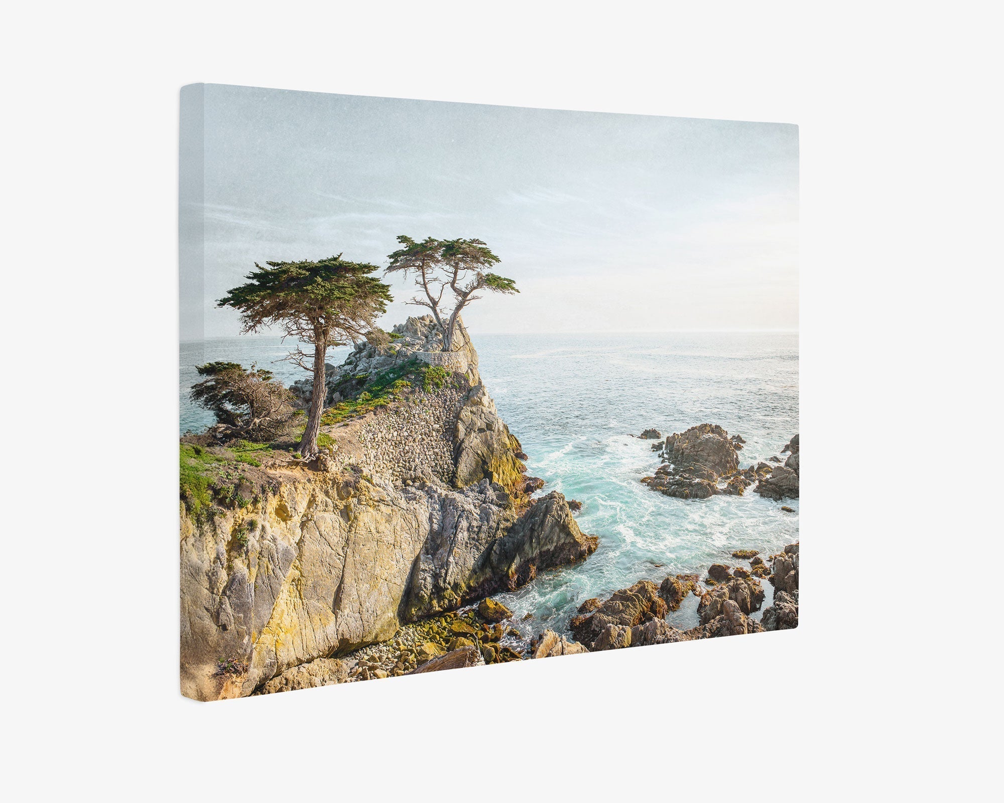 Offley Green's 30x40 Coastal Canvas Print showcases a captivating coastal scene featuring the iconic Lone Cypress perched on a rocky promontory. The ocean waves crash against the rocks under a delicately cloudy sky, complemented by sparse vegetation, creating stunning wall art that brings natural beauty into any space. Choose from over 10 unique designs to find the perfect piece for your decor.