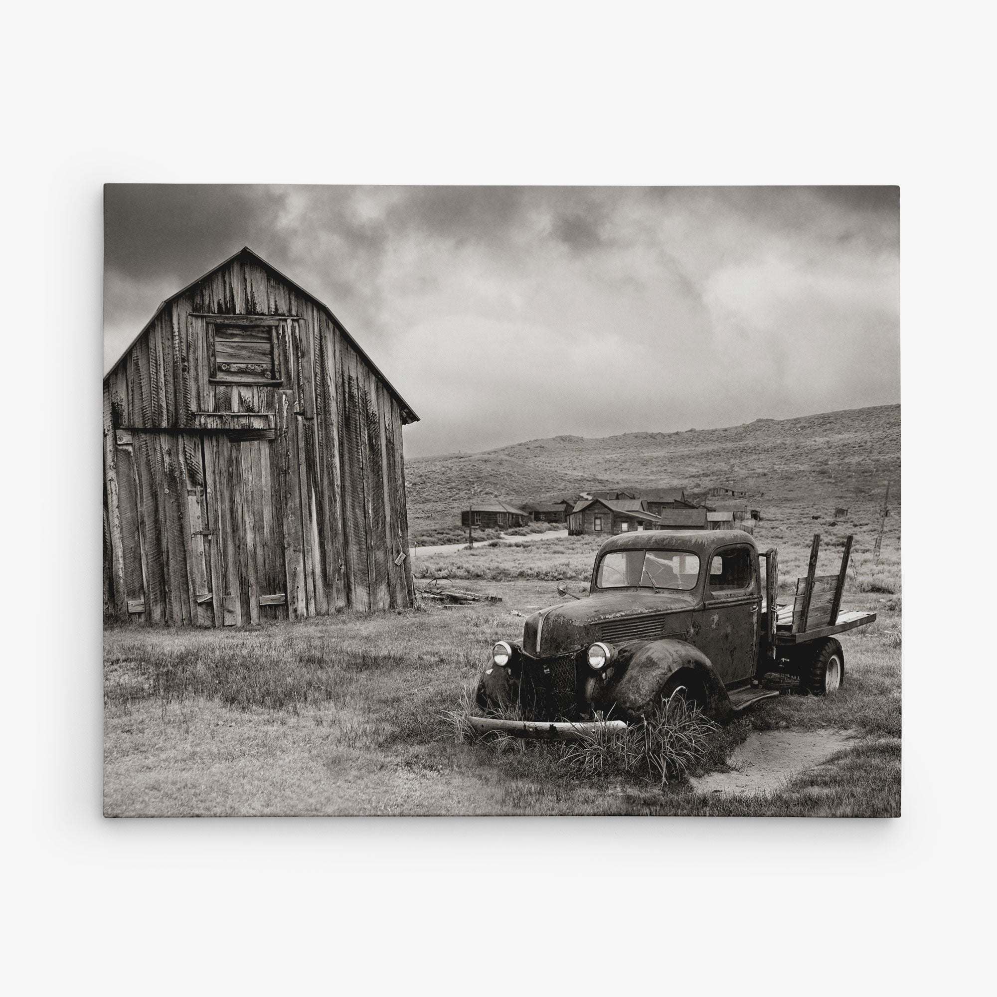 The 8x10 Rustic Canvas Print by Offley Green, featuring a sepia-toned vintage truck beside an old barn, with small buildings in a barren landscape under a cloudy sky, captures timeless charm. Perfect for gallery wraps with over 10 designs to choose from.