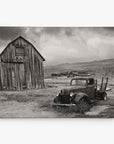 The 8x10 Rustic Canvas Print by Offley Green, featuring a sepia-toned vintage truck beside an old barn, with small buildings in a barren landscape under a cloudy sky, captures timeless charm. Perfect for gallery wraps with over 10 designs to choose from.