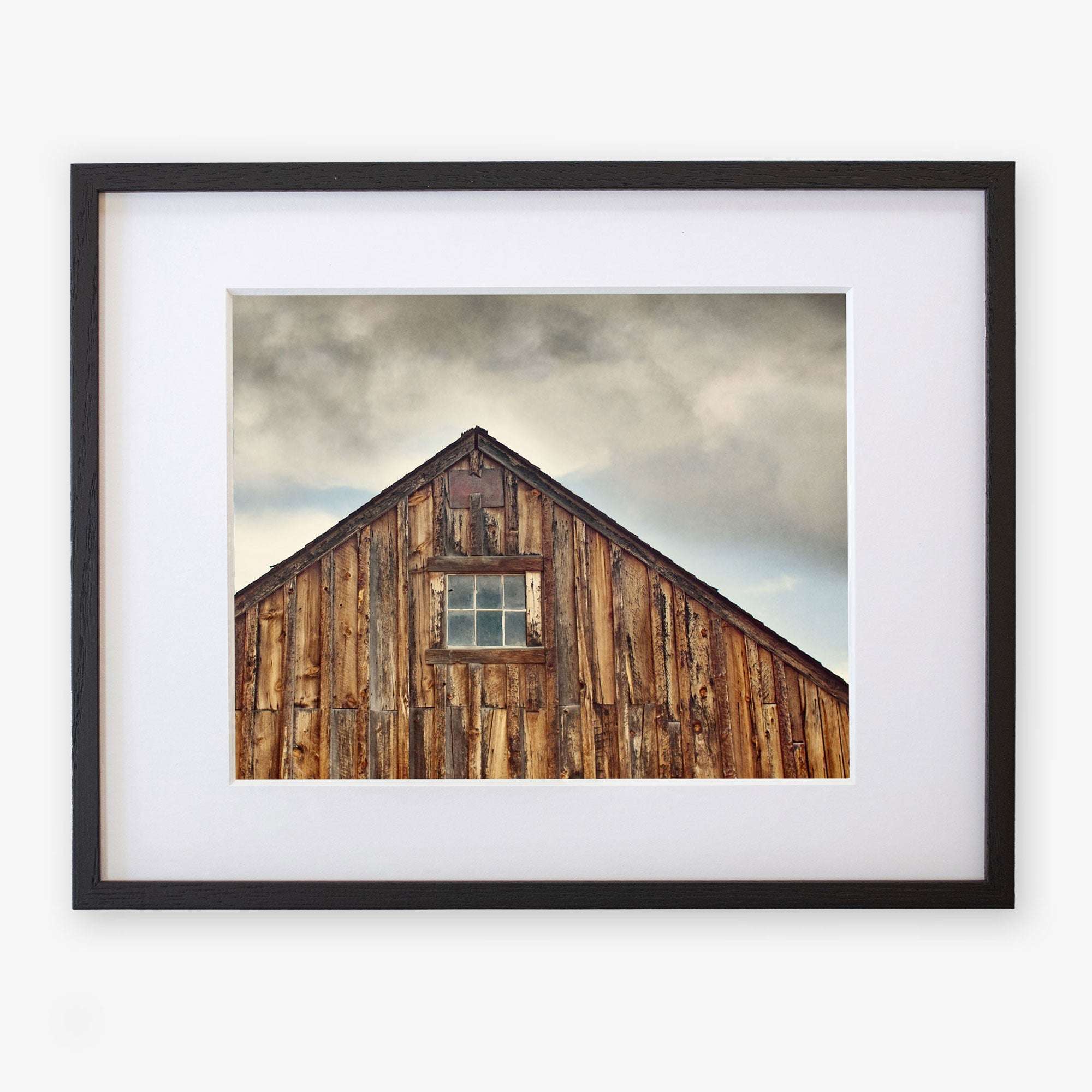 A framed photograph of an Offley Green Farmhouse Rustic Print, &#39;Old Barn at Bodie&#39;, centered and mounted on archival photographic paper, on a white gallery wall. The barn has weathered planks and a single window.