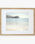 Framed photograph of a tranquil beach scene with gentle waves lapping the shore and California Beach Print, 'Malibu Pier' extending into the calm blue sea, all under a clear sky by Offley Green.