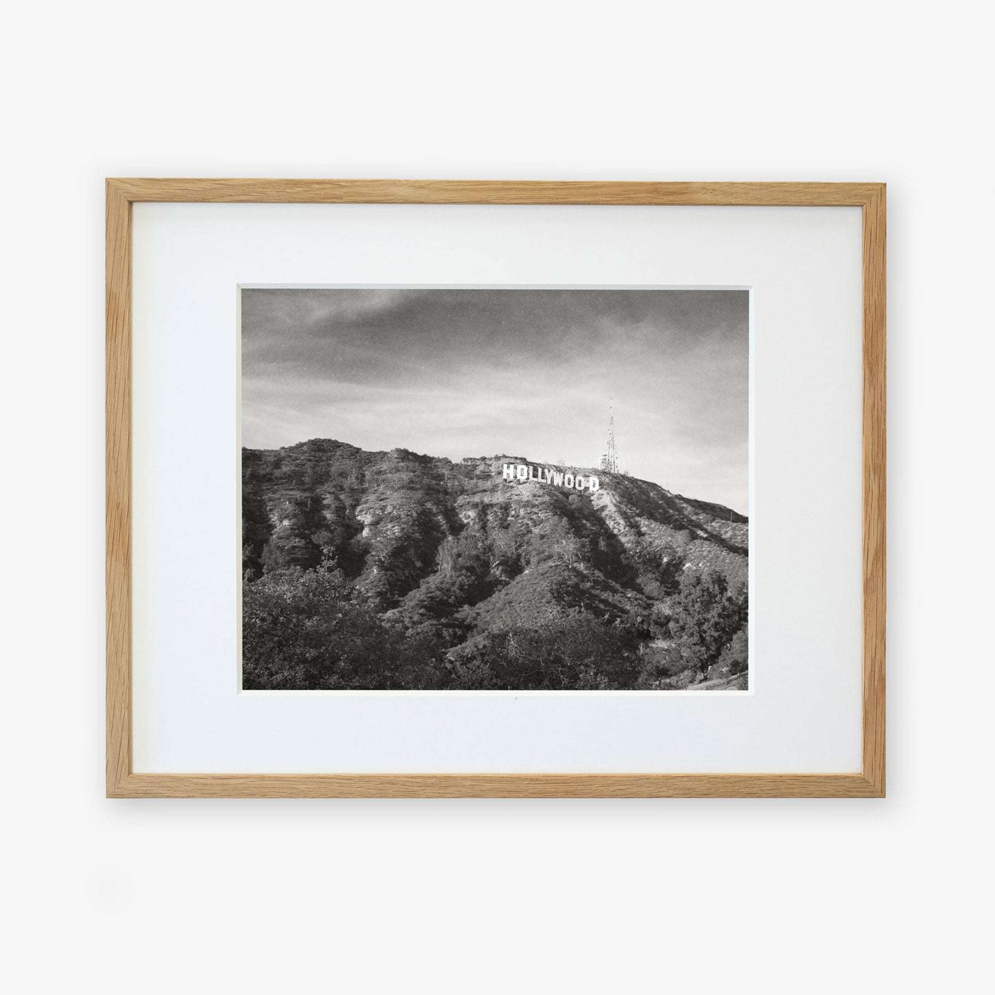 Black and white photograph of the Hollywood sign on a hill, printed on archival photographic paper, framed in a light wooden frame, against a plain white background.
Product Name: Offley Green Hollywood Sign Black and White Vintage Print, 'Old Hollywood'