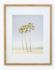 Framed artwork depicting three tall palm trees under a clear sky, with a small figure and a dog at the base, possibly on Venice Beach. The frame is simple and made of light wood. This is the Offley Green California Venice Beach Print, 'Three Palms'.
