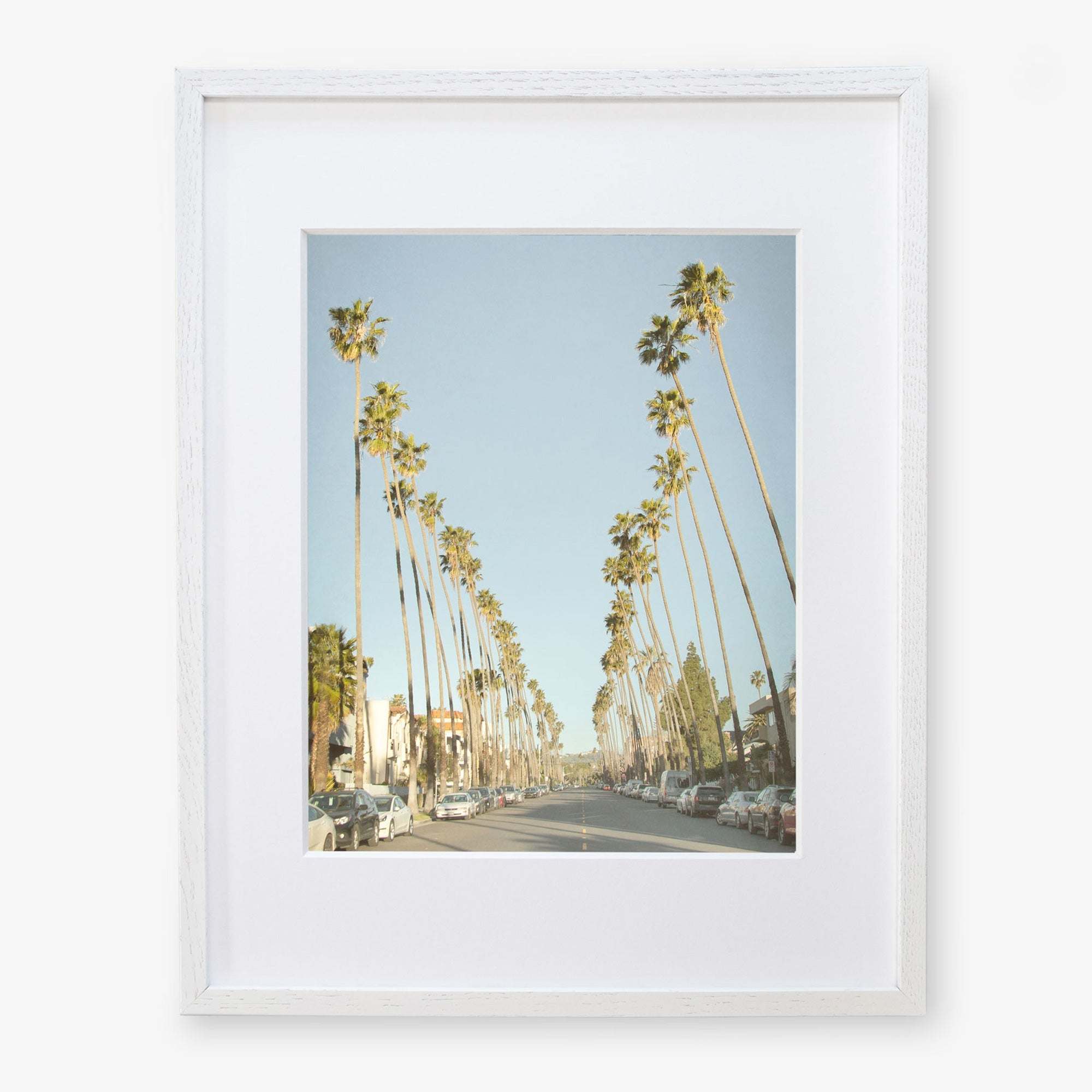 Framed photograph of Los Angeles Palm Tree Lined Street 'Sunset Boulevard Dreams' by Offley Green, cars parked along the road, and a clear blue sky.