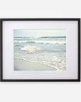 A framed photograph of a serene scene at Carlsbad State Beach, displaying gentle waves breaking near the shore with a clear sky in the background. The frame is black with a white mat featuring the Coastal Beach Print in California 'Surf and Sun' by Offley Green.