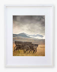 The Offley Green Rustic Farmhouse Wall Art, 'Old Wagon', features framed photography of vintage wooden wagons beneath a dramatic sky with snow-capped mountains, printed on premium photographic paper for a serene and rustic charm.