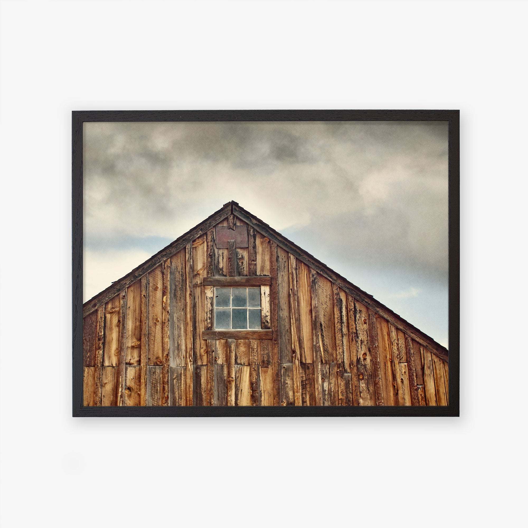 A framed photograph of the upper part of an old wooden barn with a single window, set against a cloudy sky, printed on archival photographic paper - Offley Green&#39;s Farmhouse Rustic Print, &#39;Old Barn at Bodie&#39;.