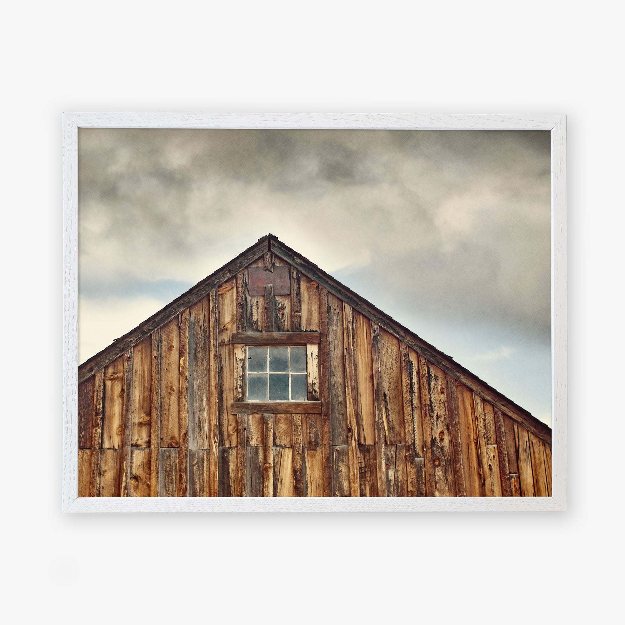 A framed photograph of an old wooden barn with weathered planks under a cloudy sky. The Offley Green &#39;Old Barn at Bodie&#39; Farmhouse Rustic Print has a small window and triangular roof peak.