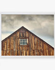 A framed photograph of an old wooden barn with weathered planks under a cloudy sky. The Offley Green 'Old Barn at Bodie' Farmhouse Rustic Print has a small window and triangular roof peak.