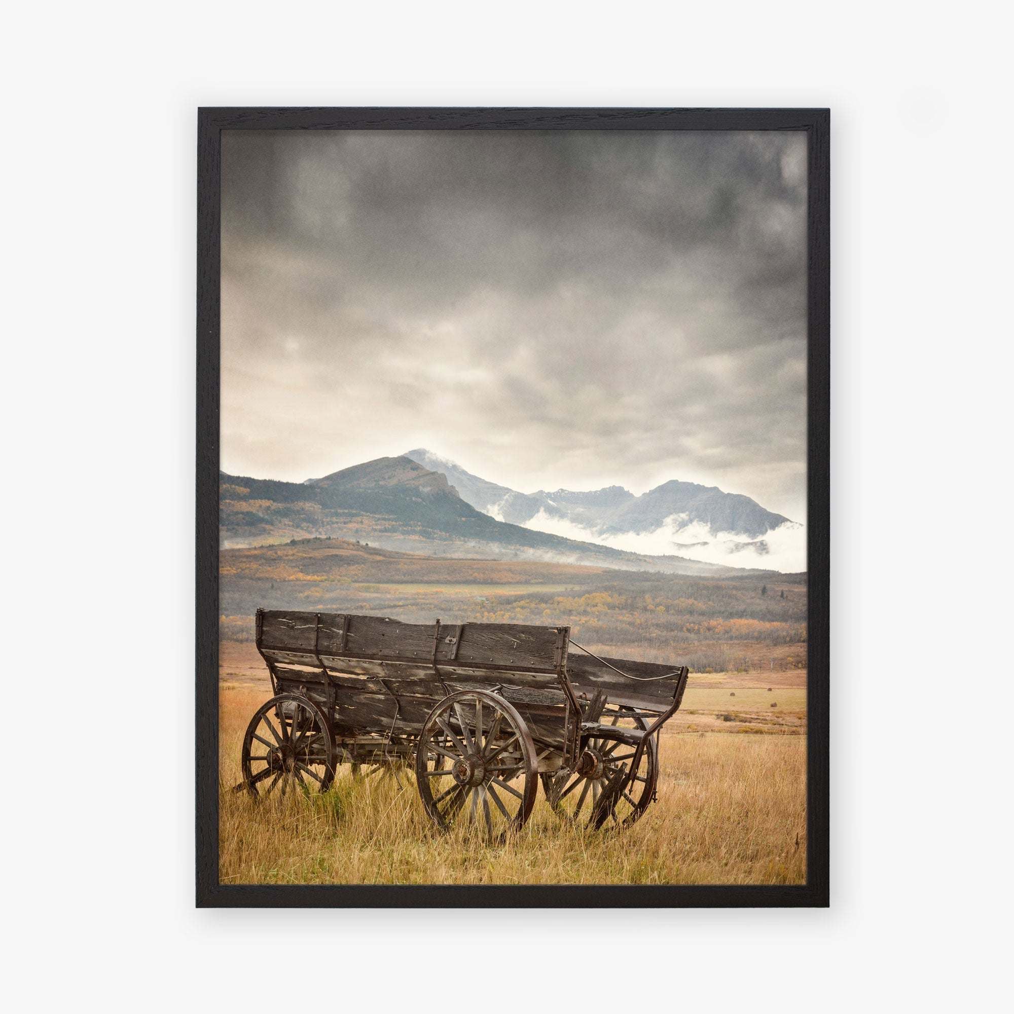 The Offley Green 'Old Wagon' Rustic Farmhouse Wall Art features a rustic wagon set in a tranquil field, with misty mountains and cloudy skies enhancing its timeless charm.