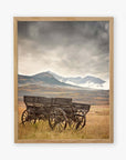 The "Rustic Farmhouse Wall Art, 'Old Wagon'" by Offley Green features a framed image of a weathered wooden wagon in a grassy field, set against rolling hills and snow-capped mountains beneath a cloudy sky.