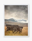 Offley Green's "Rustic Farmhouse Wall Art, 'Old Wagon'" beautifully captures a ruined wagon on grassy plains under a cloudy sky with snow-capped mountains in the background, adding rustic charm to this dramatic landscape on photographic paper.