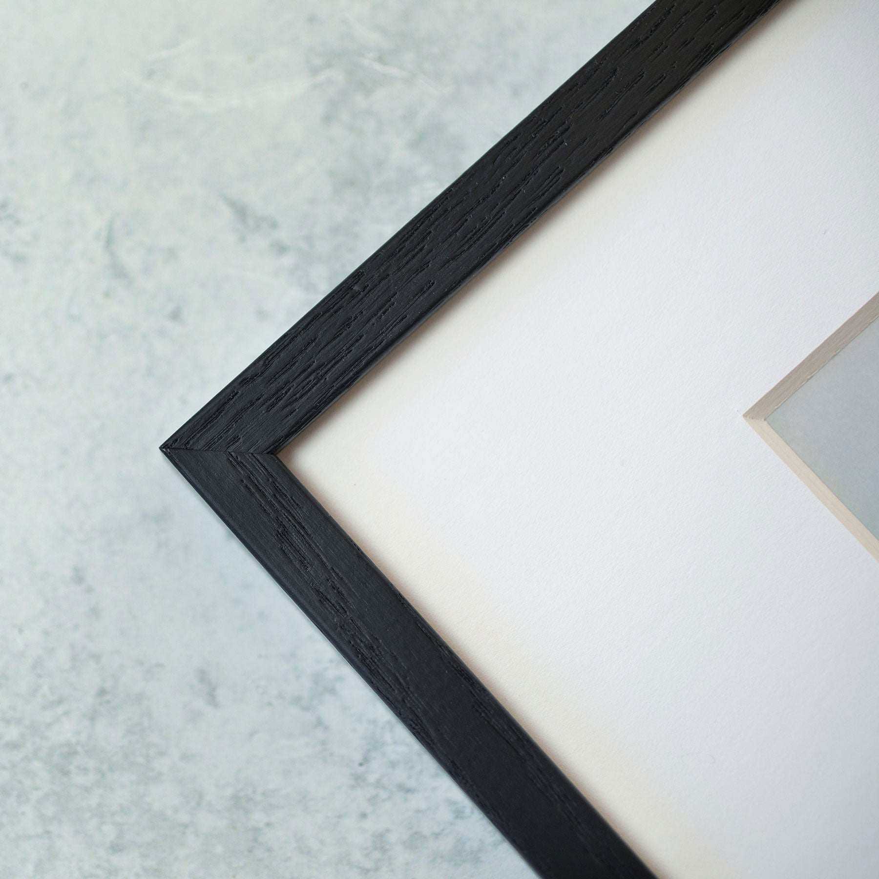 A corner of the Rustic Farmhouse Wall Art, 'Old Wagon' by Offley Green is shown against a light gray textured background. The black frame with a white mat displays a small part of the artwork, exuding rustic charm.