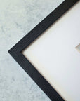 A corner of the Rustic Farmhouse Wall Art, 'Old Wagon' by Offley Green is shown against a light gray textured background. The black frame with a white mat displays a small part of the artwork, exuding rustic charm.