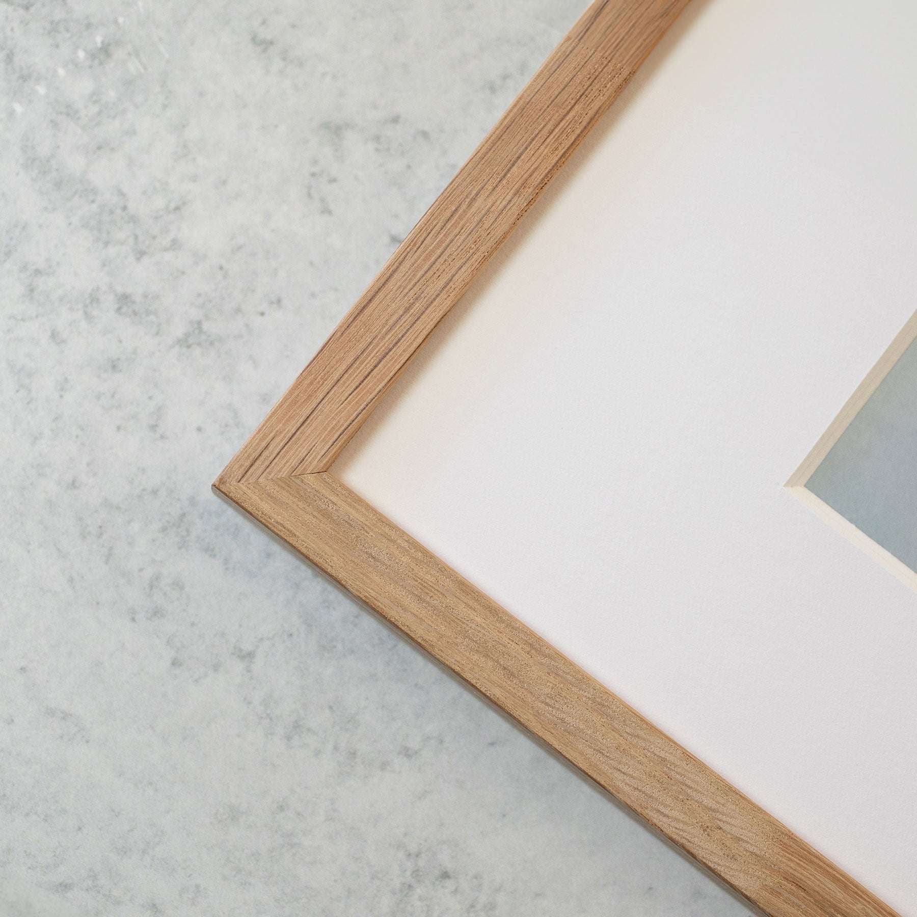 Close-up of a wooden picture frame on a pale marble background, focusing on the frame&#39;s corner and part of the white matte inside, containing Offley Green&#39;s &#39;Strands and Spikes II&#39; green botanical print.
