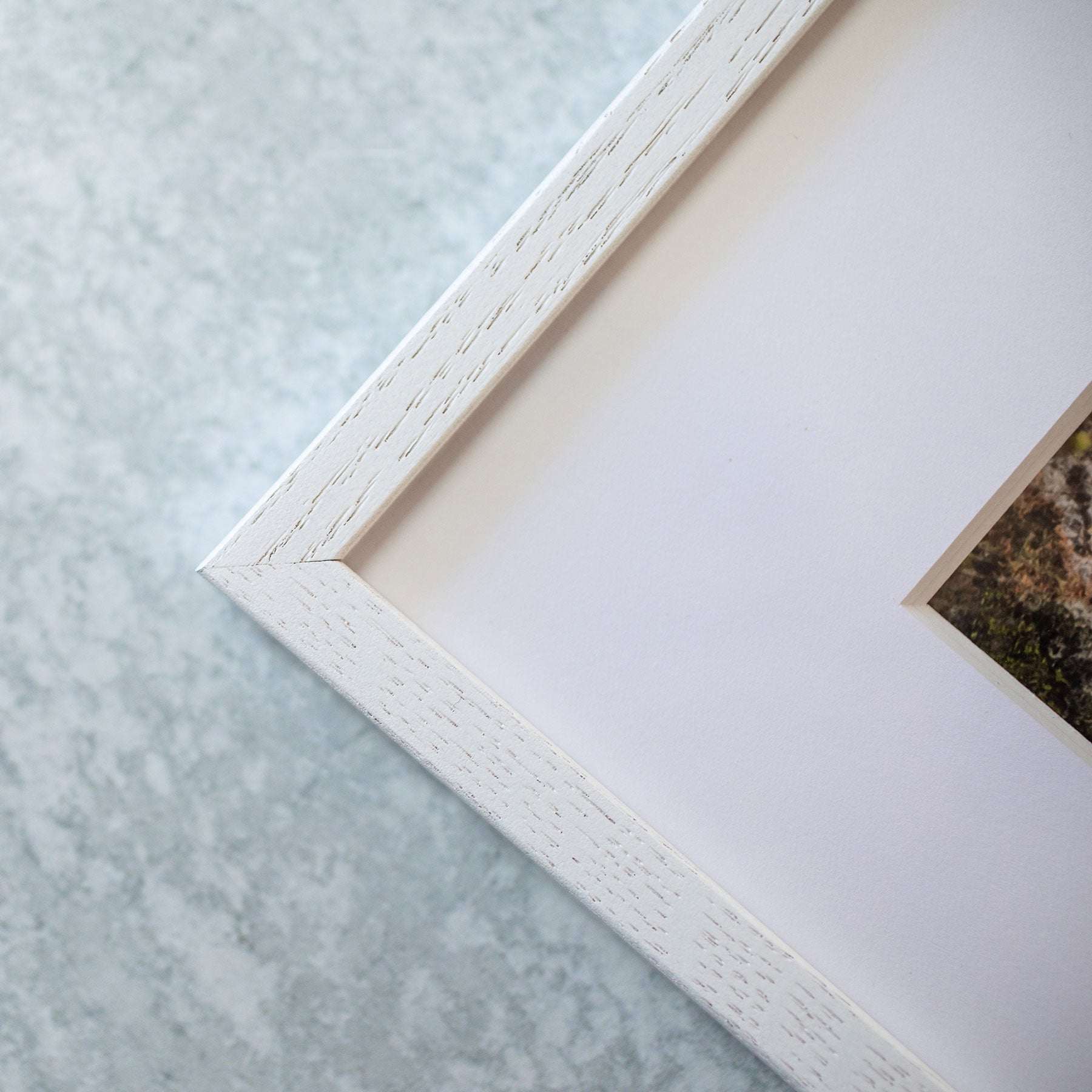 Close-up of a corner of a white textured Offley Green picture frame against a light gray background, showcasing detailed craftsmanship on archival photographic paper with the Big Sur Landscape Print, &#39;Lobster Mornay For Tea&#39;.