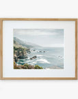 A framed wall art featuring a picturesque coastal scene from Big Sur, with cliffs, the ocean, and distant fog. The light wooden frame complements the serene coastal colors. - Offley Green's Big Sur Landscape Print, 'Rocky Rocks'