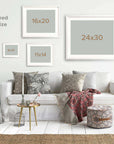A rustic living room features a white sofa with patterned cushions and a woven throw. Overhead, 'Old Wagon' by Offley Green, framed on photographic paper in various sizes, adds charm. The decor is completed with a jute rug, small side tables, and a pouf.