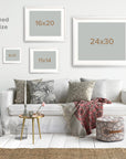 A cozy living room features a white sofa adorned with patterned pillows and a red throw blanket. Above the sofa are prints of Offley Green's Rustic Floral Print, 'Fields of Lavender' in various sizes: 8x10, 11x14, 16x20, and 24x30. Decorative elements include side tables, a lamp, plants, and a woven pouf. Text reads "Unframed Print Size Guide.