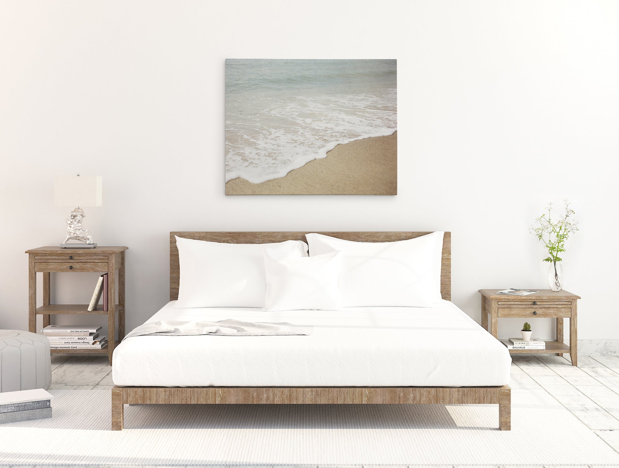 Minimalist bedroom with a wooden bed frame and white bedding. A nightstand on each side of the bed features a small decor item and lamp. A large 30x40 Coastal Canvas Print by Offley Green hangs as wall art above the bed, and a vase with flowers adorns the right nightstand.