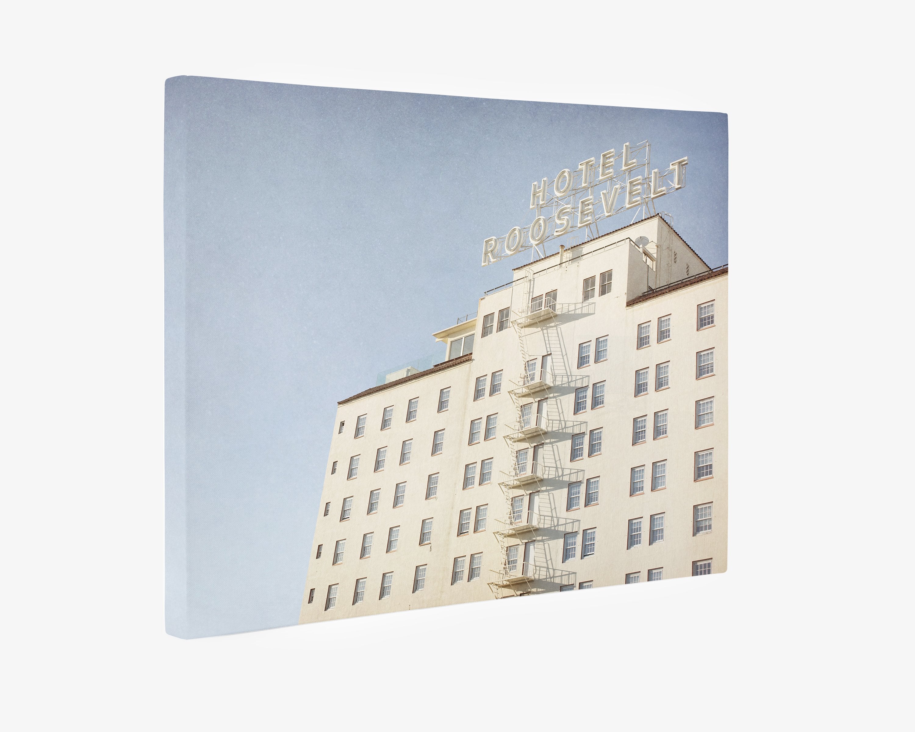 A Retro Hollywood Canvas Wall Art of the Roosevelt Hotel Hollywood by Offley Green, featuring the building&#39;s off-white facade with a fire escape, under a clear sky. The hotel name is displayed at the top in bold letters.