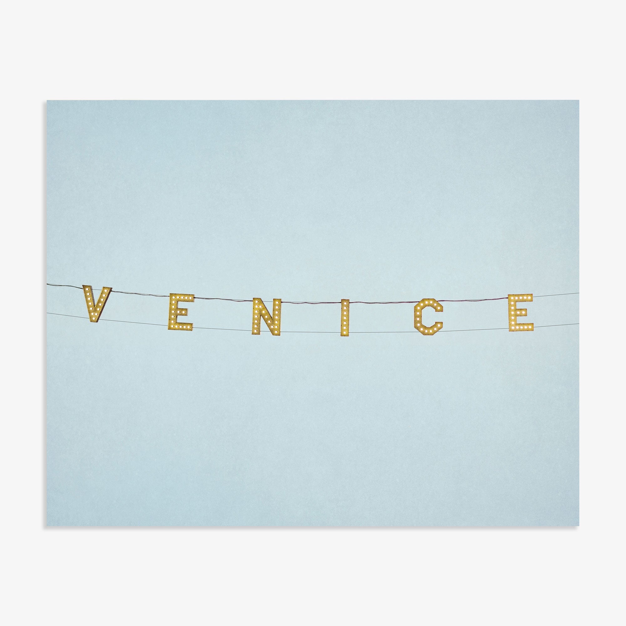 A minimalist representation with the Venice Beach Sign Print, &#39;Blue Venice&#39; spelled out in yellow letters on small flags strung across a plain light blue background, printed on archival photographic paper by Offley Green.