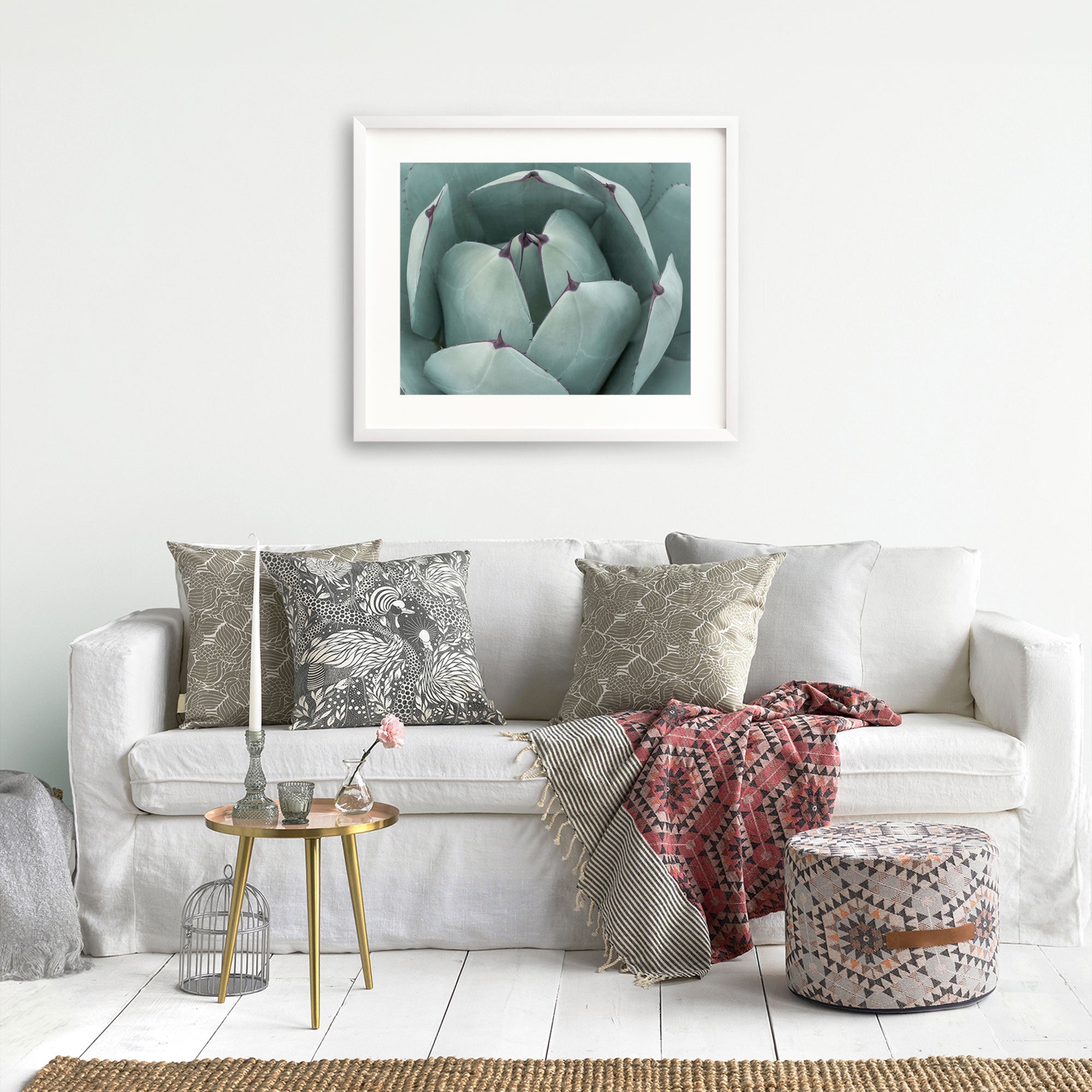 A cozy living room featuring a white sofa with decorative gray and black pillows, an Abstract Teal Green Botanical Print, &#39;Teal Petals&#39; by Offley Green above it, a small round table with books, and a red patterned throw