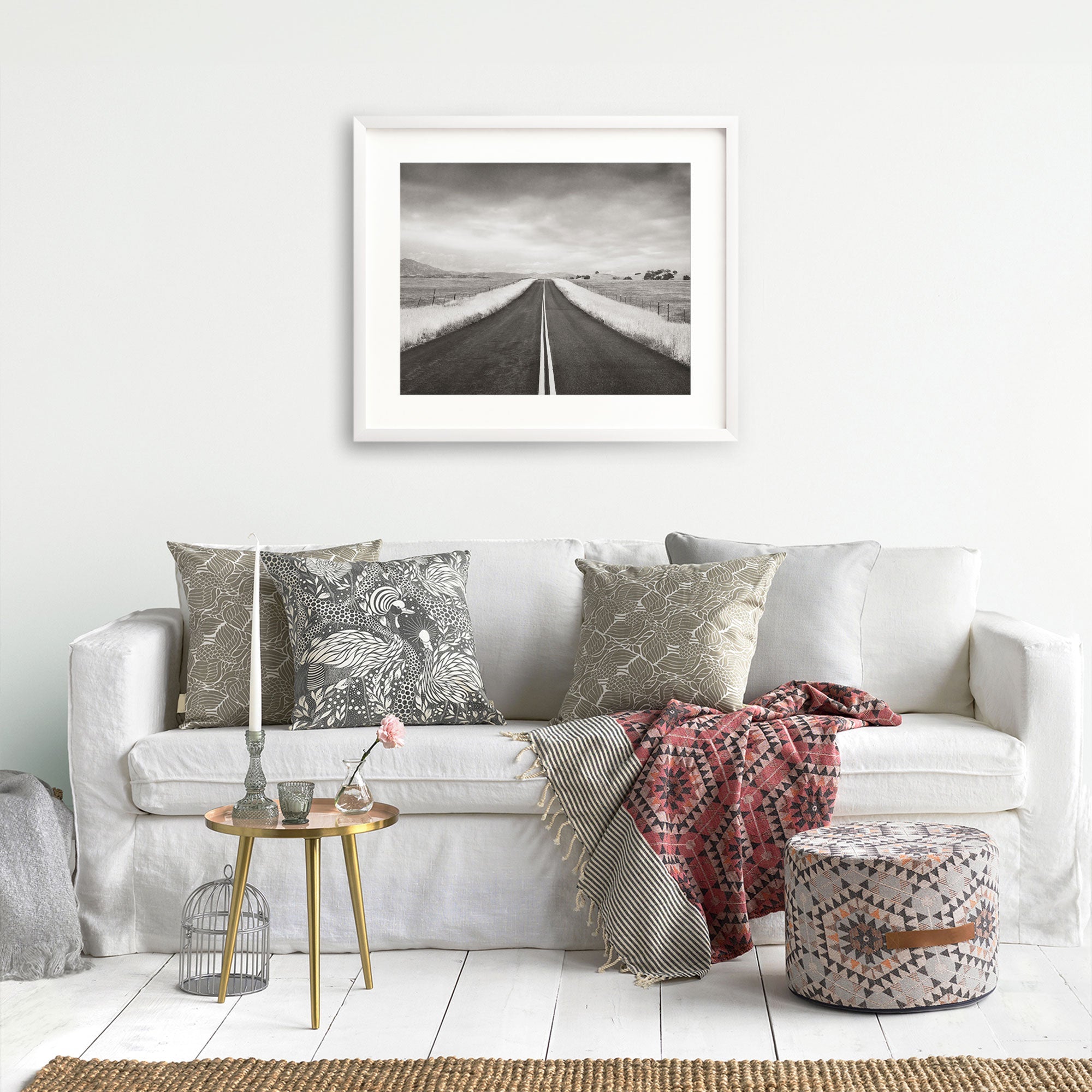 A cozy living room featuring a Offley Green black and white rural landscape art piece titled 'American Road Trip' hangs on the wall above the sofa.