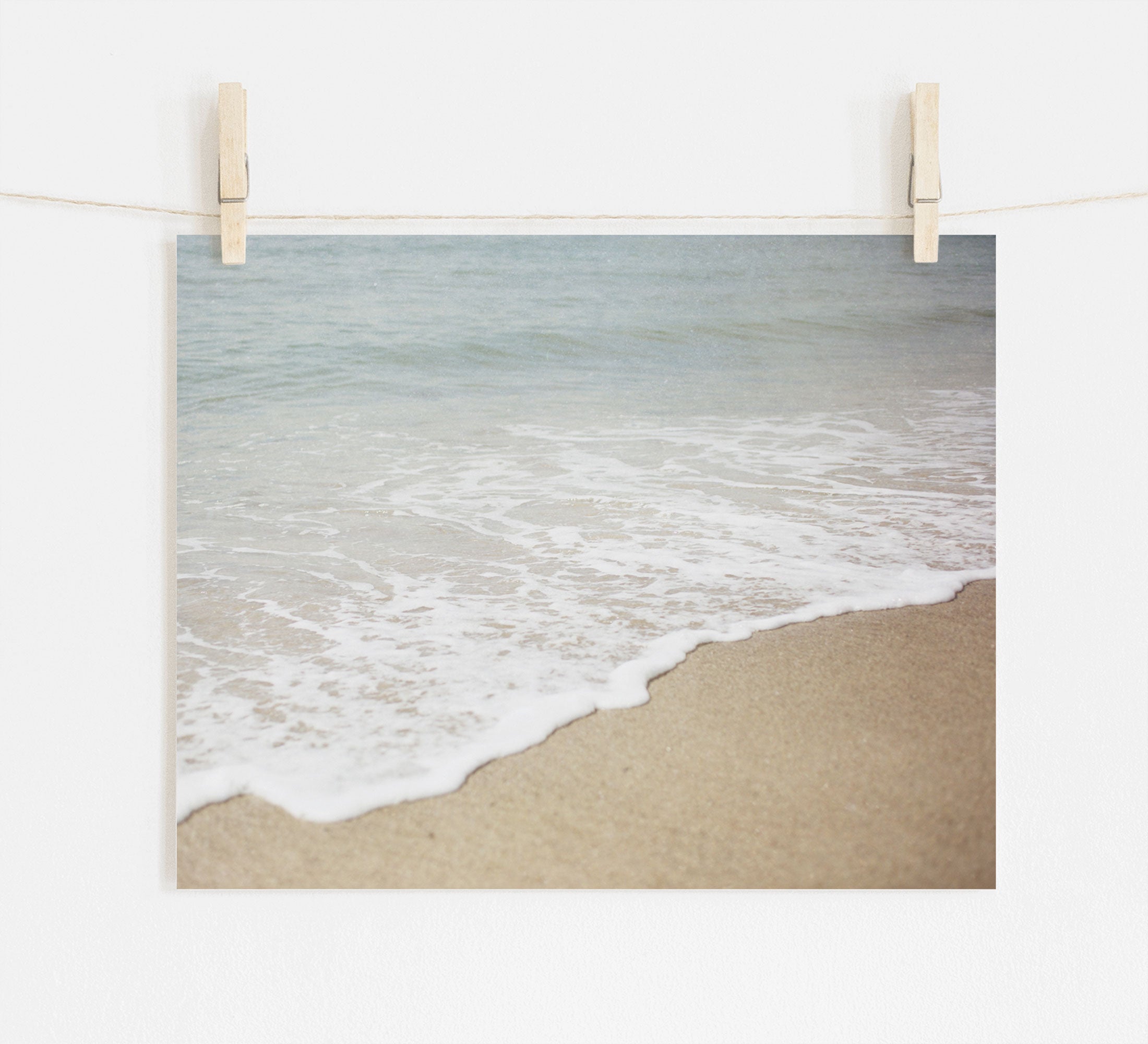 A photograph of a Beach Waves Print, 'Chasing Surf' by Offley Green, printed on archival photographic paper and pinned up by two wooden clothespins on a string against a white background.