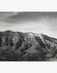 Black and white photograph of the Hollywood Sign Black and White Vintage Print, 'Old Hollywood' on a hill, printed on archival photographic paper, with textured clouds above and lush foliage covering the slopes by Offley Green.