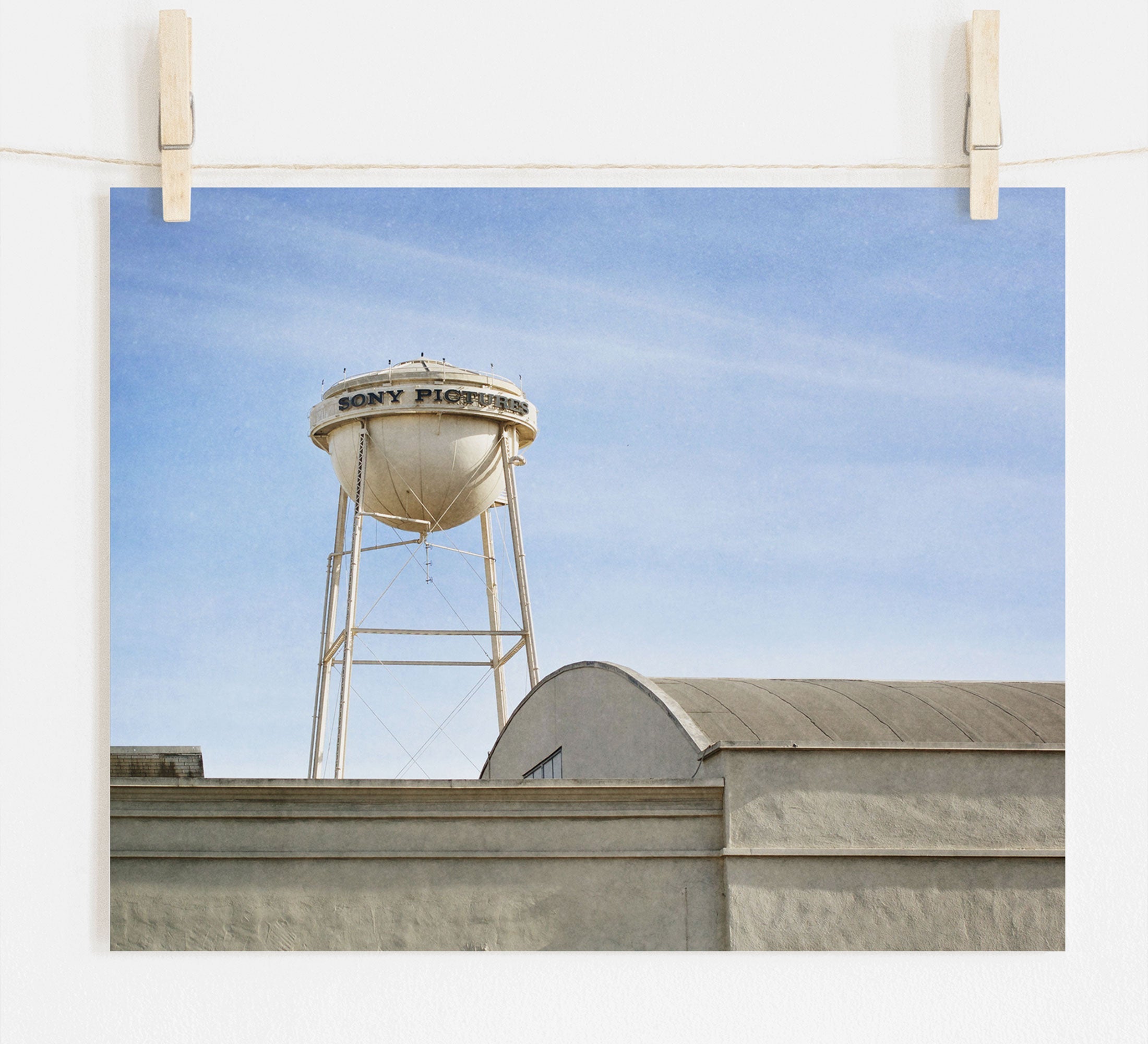 A photo of a water tower labeled &quot;Sony Studios&quot; against a clear sky, seemingly displayed as an unframed print hanging by clips on a wire. This is the Los Angeles Sony Pictures Studio Print by Offley Green, also known as the &#39;Sony Lot&#39; print.