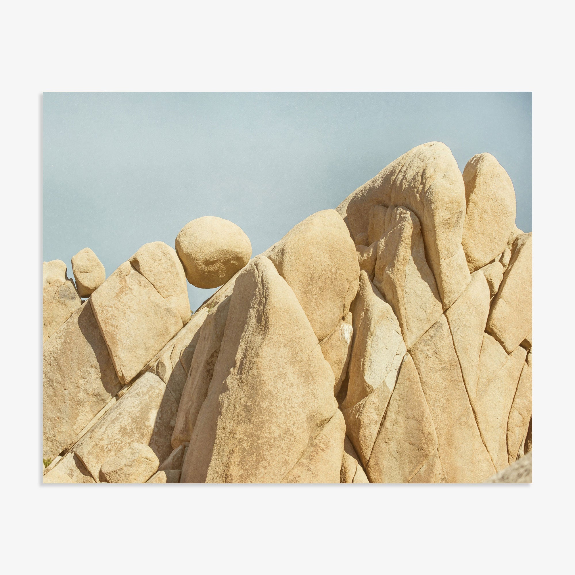 A series of large, smooth beige rocks in Joshua Tree National Park under a clear blue sky, closely packed and showing varying shapes and textures, resembling a rugged mountain landscape. The Offley Green &#39;Rock Formations&#39; Joshua Tree Print captures the stunning beauty of this iconic park.