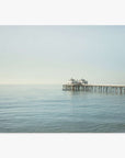 A tranquil seascape featuring Offley Green's 'Coastal Print of Malibu Pier in California "All Calm in Malibu" extending into calm waters with a large structure at the end under a clear sky.