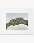 Offley Green's Los Angeles California Print, 'Santa Monica Pier Blues' featuring the Santa Monica Pier sign with words "sport fishing boating cafes" against a cloudy sky, displayed in a white frame.