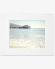 A serene beachscape featuring gentle waves washing ashore, with the Offley Green California Beach Print, 'Malibu Pier' extending into the sea under a clear blue sky, framed as a polaroid photo.