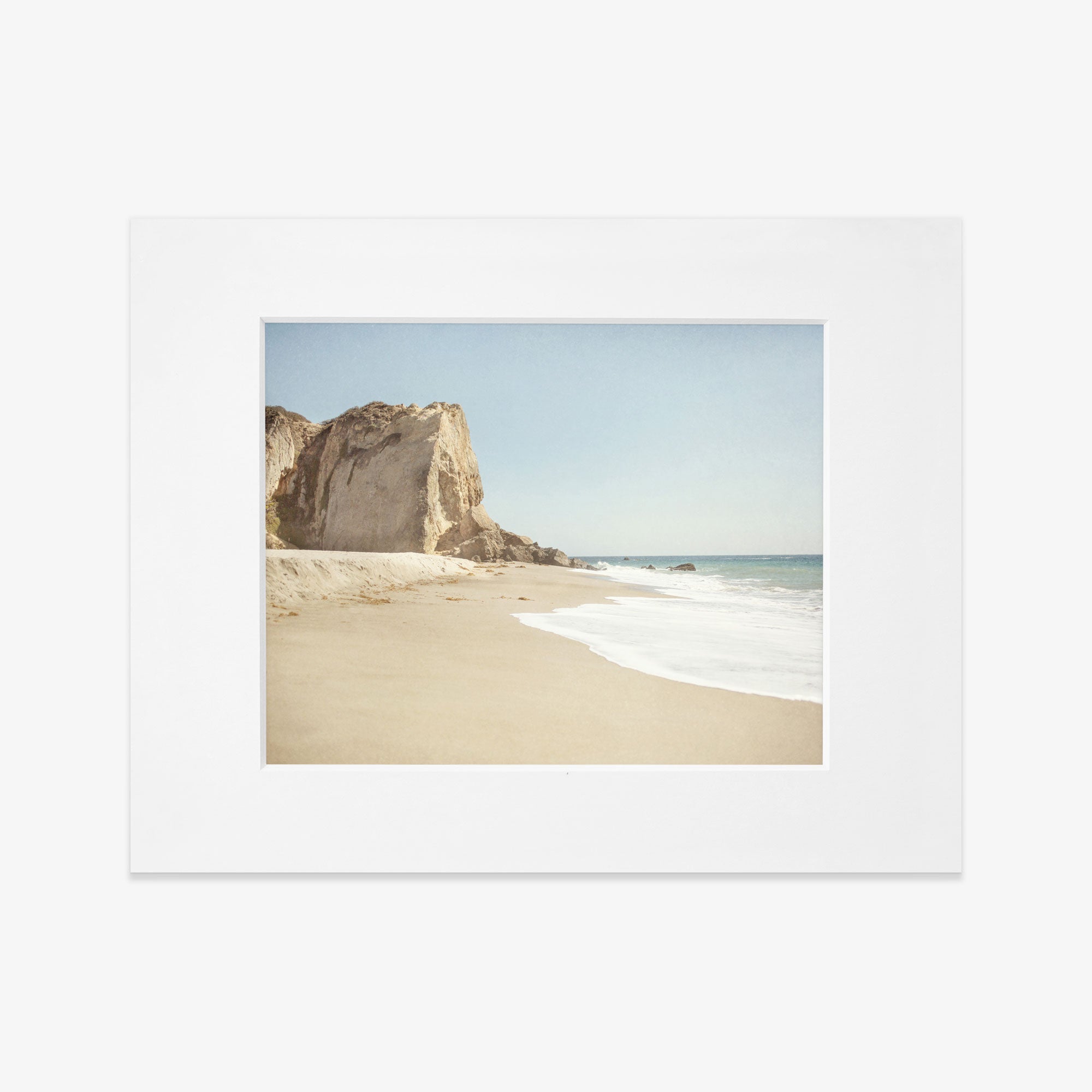 A Offley Green California Malibu Print, &#39;Point Dume&#39; of Point Dume beach with a large rock formation on the left, gentle waves, and a clear sky, placed on a white background.